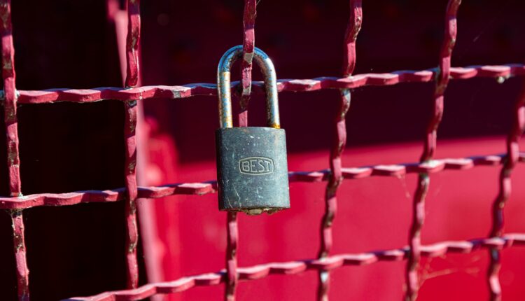 brass padlock on red metal fence